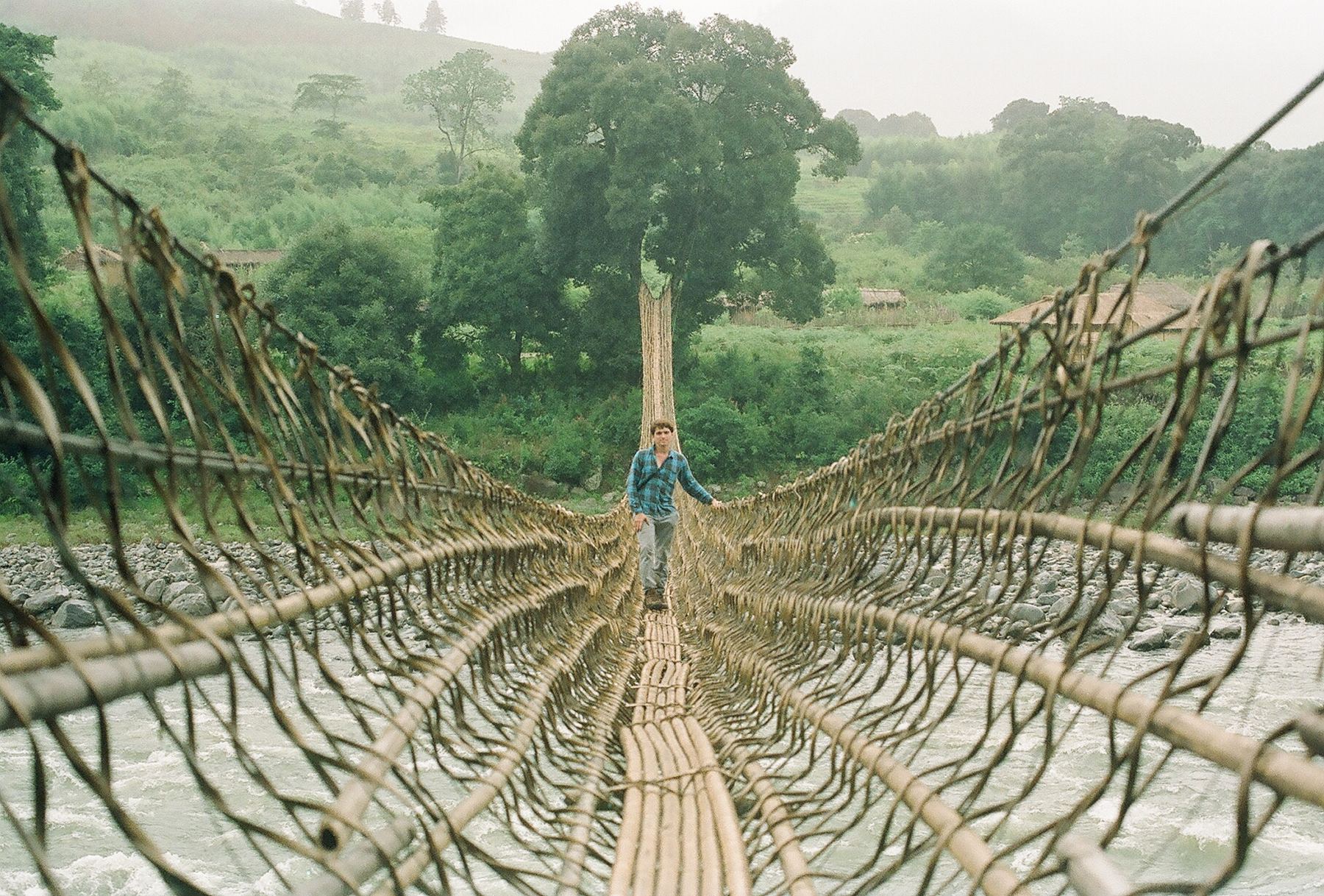 A long cane suspension bridge over a river in the mist