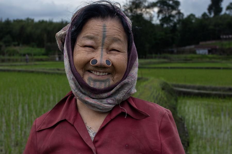 A smiling Apatani elder in front of rice fields